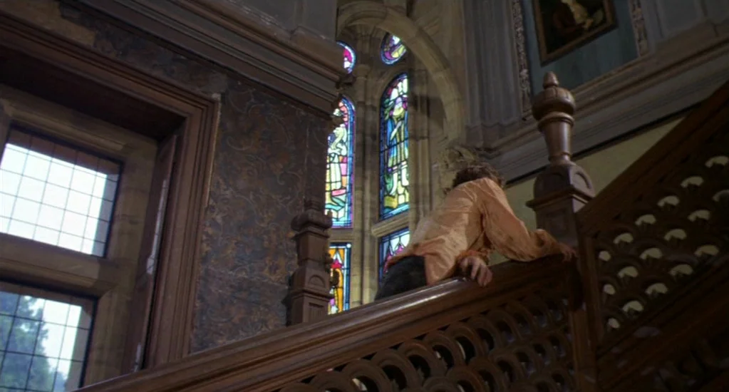 Demons of the Mind (1972) movie still: medium — A grand interior with dark carved wooden railings and ornate stained glass windows. A person moves…