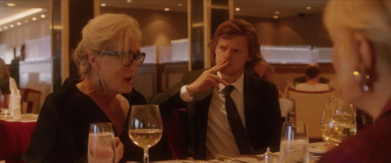 Let Them All Talk movie still: medium — An upscale dining room features red booths and polished tables under warm lighting. A woman talks to a man…