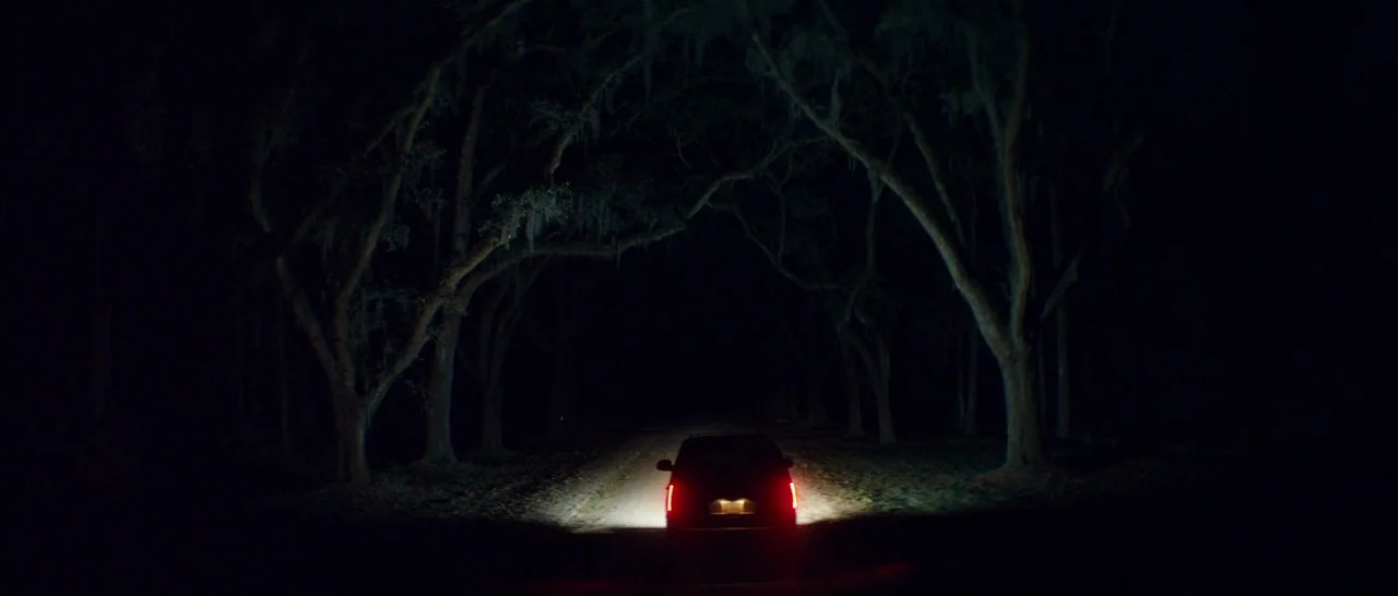 Magic Mike XXL (2015) movie still: wide — A dark country road is framed by tall trees covered in Spanish moss. A car drives away into the distance,…