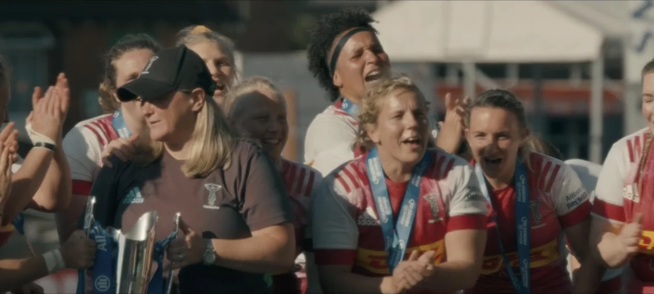 No Woman No Try (2022) movie still: medium — A group of female athletes in rugby jerseys celebrate on a sports field. Several women clap and cheer…