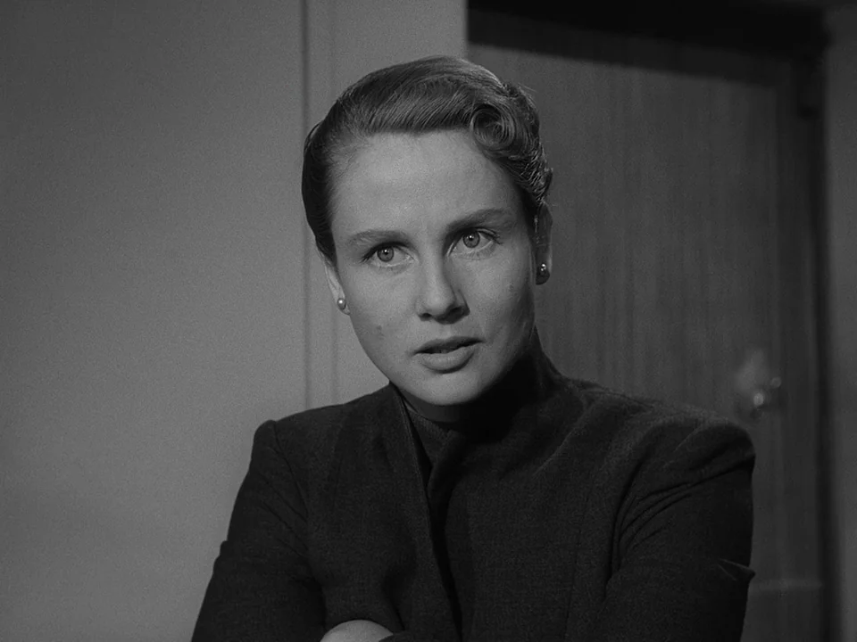 Brink of Life (1958) movie still: closeup — A woman is positioned indoors before a plain wall and a wooden door. She looks toward the camera while…
