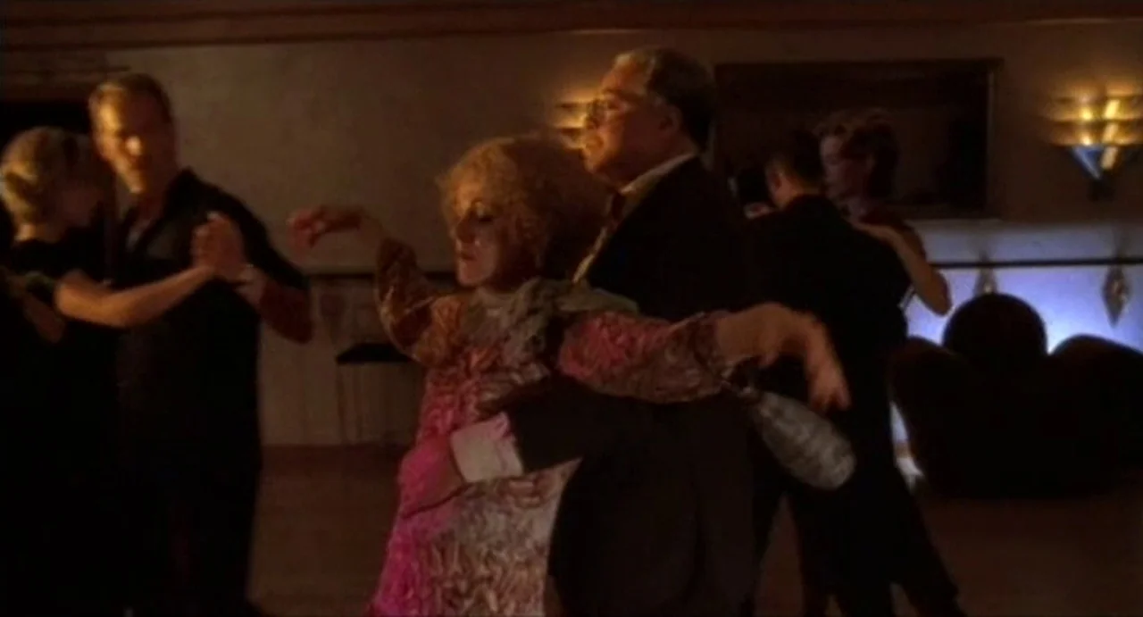 The Annihilation of Fish (1999) movie still: medium — A dimly lit room functions as a dance space with wall-mounted lamps glowing softly. A man and…