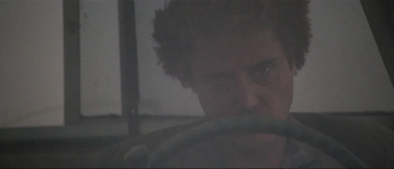 At Close Range (1986) movie still: closeup — A man sits behind the steering wheel inside the cabin of an old vehicle. Hazy light fills the space…