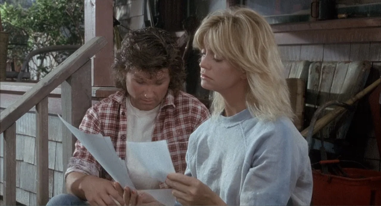 Overboard (1987) movie still: medium — A wooden porch area features shingled siding and weathered outdoor equipment in the background. A man and a…