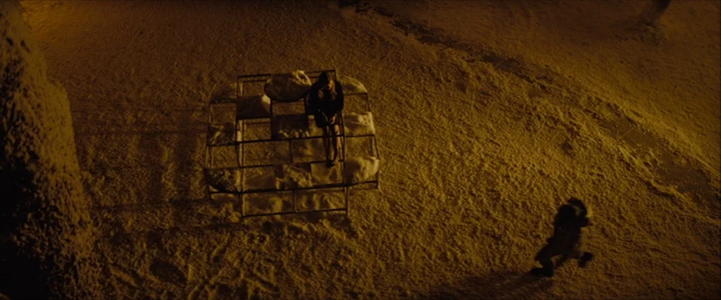 Let Me In (2010) movie still: wide — A snowy outdoor area at night with a metal jungle gym frame. One person sits on the apparatus while another…