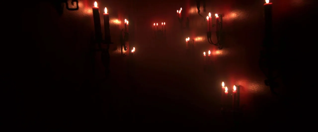 Insidious (2010) movie still: establishing — A dark hallway features red walls and several ornate wrought-iron candle sconces. Flickering candles…