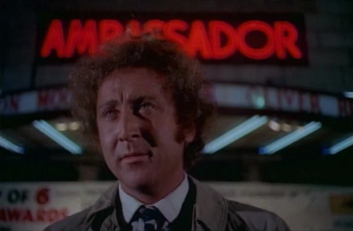 Quackser Fortune Has a Cousin in the Bronx (1970) movie still: closeup — A man stands before the red glowing neon sign of the Ambassador theater…