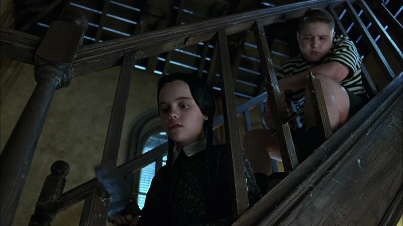 Addams Family Values (1993) movie still: medium — A wooden staircase in an old house with dust-covered banisters and dark slats. A girl with dark…
