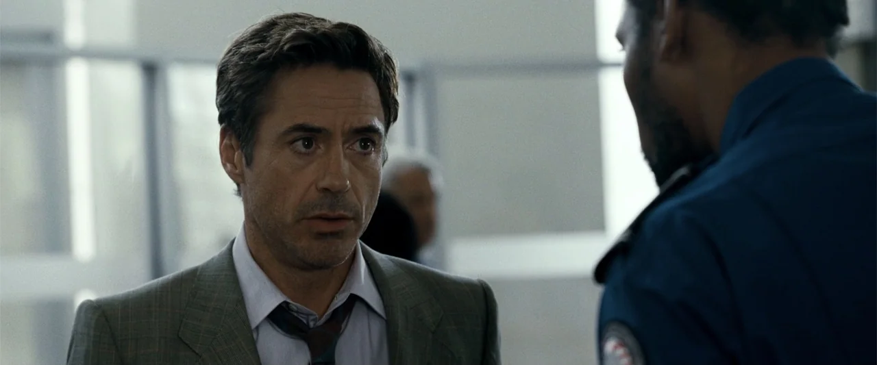 Due Date (2010) movie still: medium — A modern building interior features glass wall partitions and minimalist professional decor. A man in a suit…