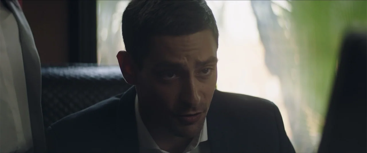 Redemption Day (2021) movie still: closeup — An office interior with blurred light reflecting through a window in the background. A man in a suit…