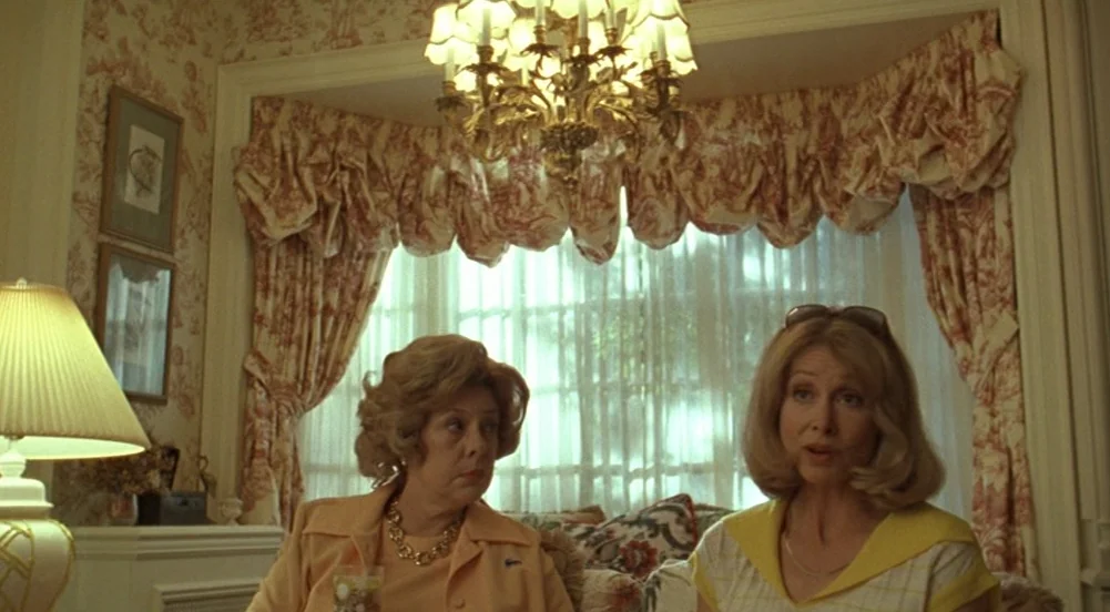 The Virgin Suicides (1999) movie still: medium — A sunroom features toile wallpaper and heavy patterned curtains draped over a large window. Two…