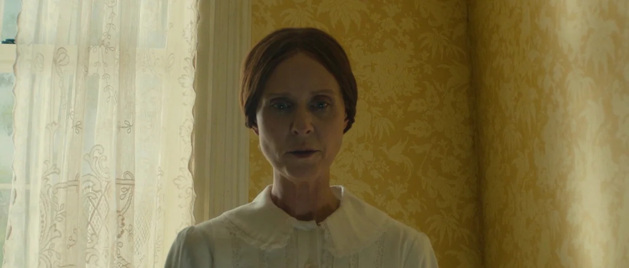 A Quiet Passion (2016) movie still: medium — A room with patterned yellow wallpaper sits beside a window with sheer white curtains. A woman wearing…