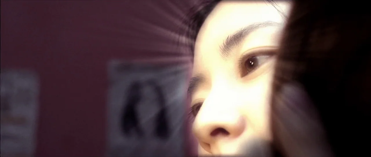 Lady Vengeance (2005) movie still: closeup — A dimly lit room with purple-toned walls featuring blurred posters in the background. A young woman is…