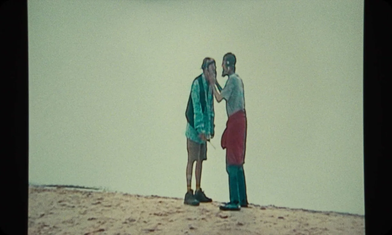 Vulcanizadora (2024) movie still: fullbody — Two individuals stand against a stark, featureless white background on a sandy surface. One person…