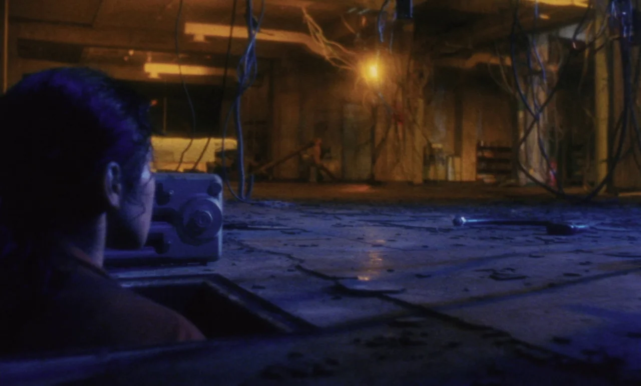 Evil Dead Trap (1988) movie still: medium — A dark subterranean space filled with hanging wires and cracked concrete flooring. A person looks out…