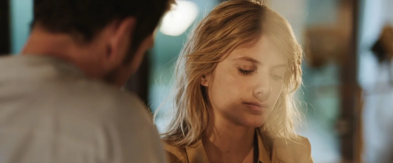 Mia and the White Lion (2018) movie still: medium — An interior space contains a woman sitting in focus across from a blurred man. The woman looks…