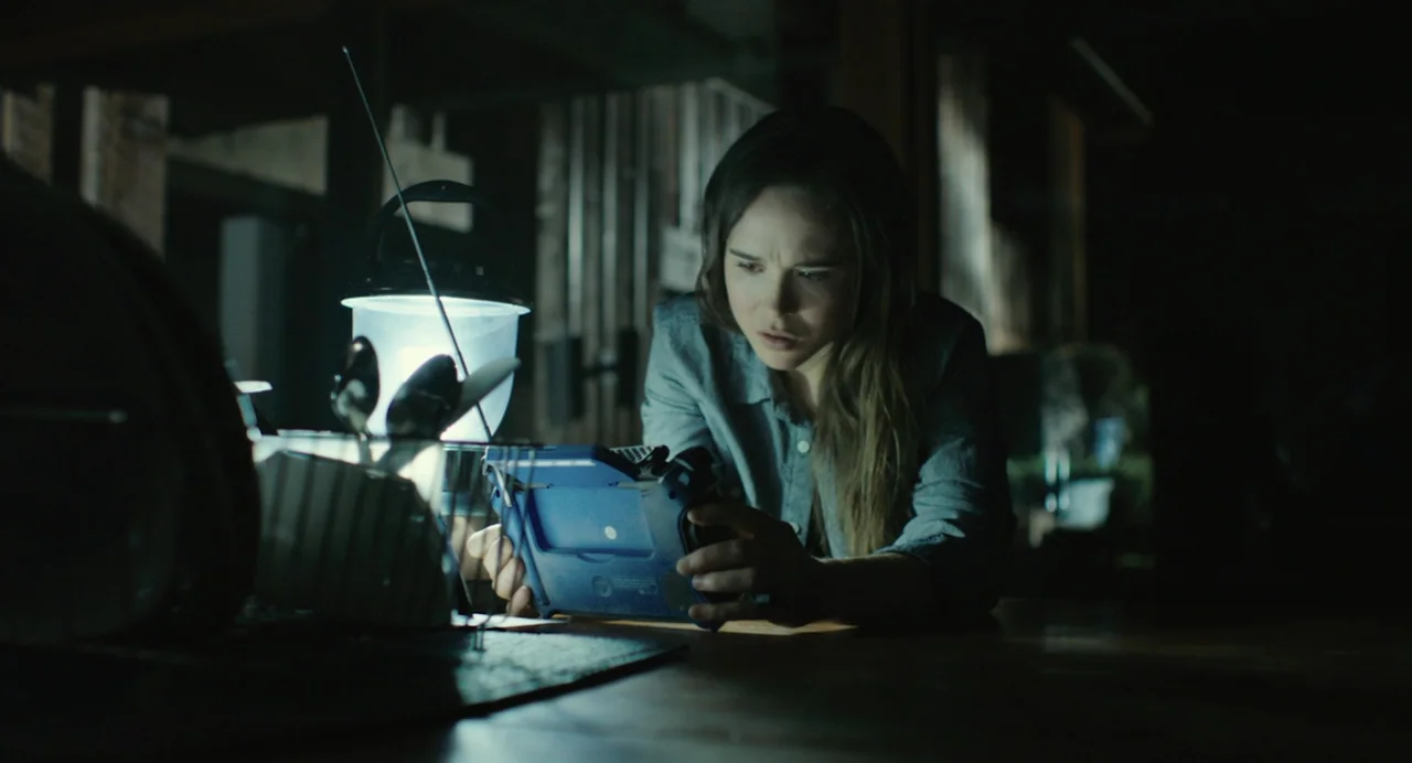 En lo profundo del bosque movie still: medium — A dimly lit room at night with a table surface and dark surroundings. A young woman focuses…