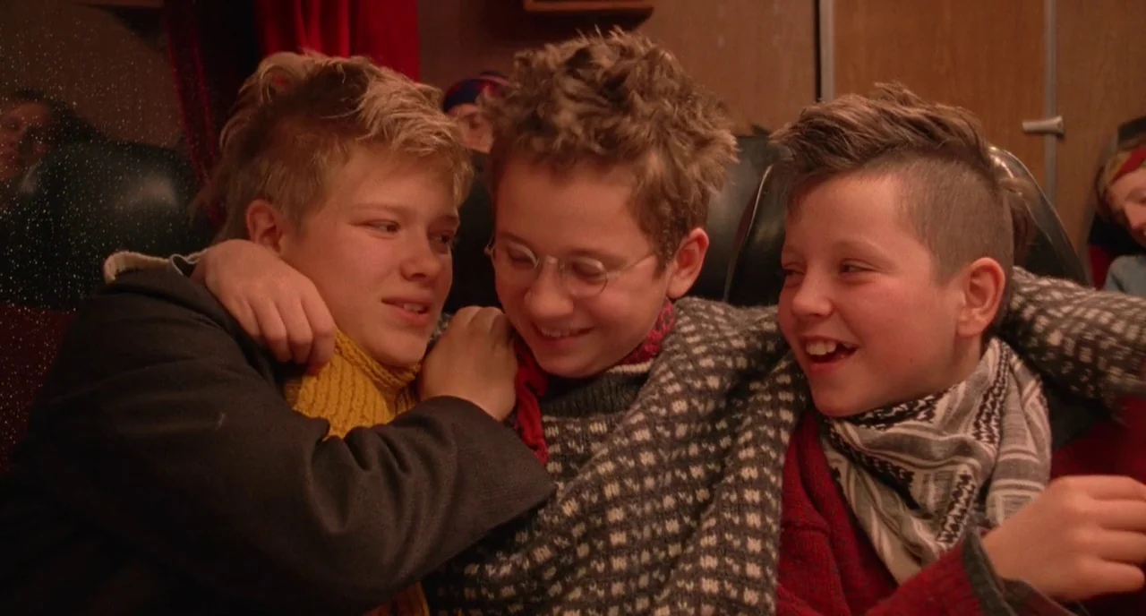 We Are The Best! (2013) movie still: medium — Three adolescents sit together in a cramped row of upholstered bus seats. They are huddled in a group…