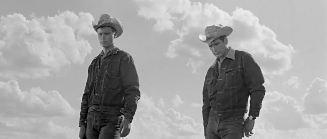 Hud (1963) movie still: fullbody — An open field under a bright sky filled with scattered white cumulus clouds. Two men wearing denim jackets and…