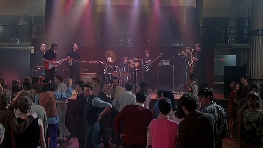 The Unbearable Lightness of Being (1988) movie still: wide — A spacious dance hall features a raised wooden stage with a performing band. The…