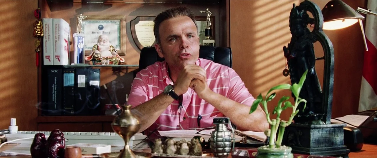 Bad Boys II (2003) movie still: medium — A wood-paneled office workspace features numerous awards and figurines on the shelves. A man in a striped…