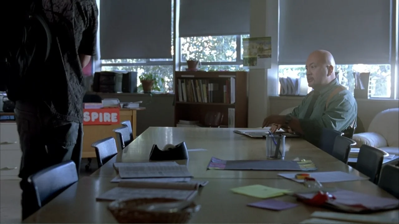 Paranoid Park (2007) movie still: medium — A school office contains a wooden conference table with papers, pens, and chairs arranged inside. A man…