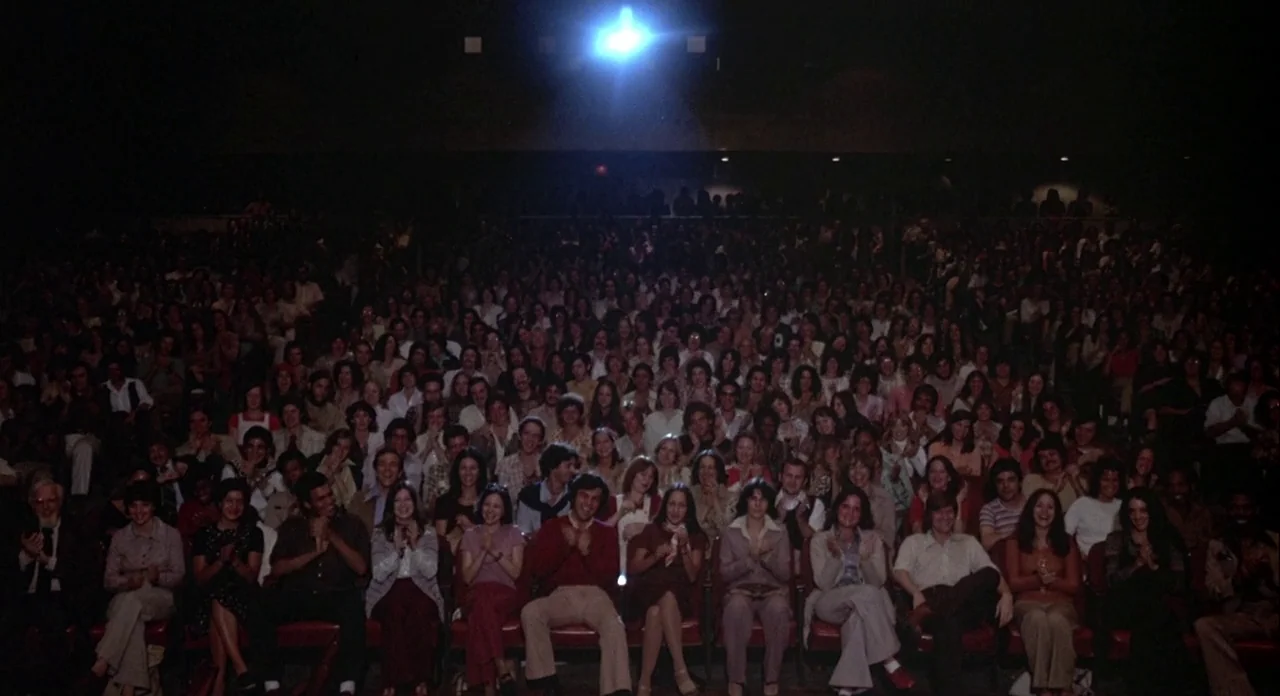 Annie Hall (1977) movie still: wide — A crowded movie theater auditorium filled with people sitting in rows of red seats. The audience members are…