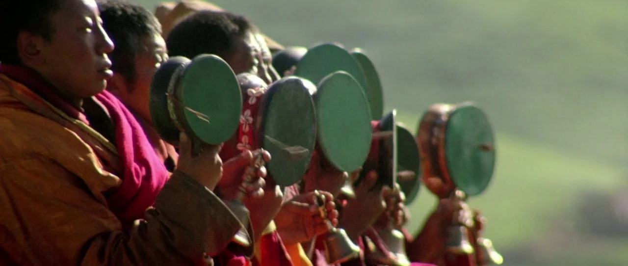 Horse Thief movie still: medium — A group of monks in traditional robes stand in a row outdoors. They hold green circular hand drums and small brass…