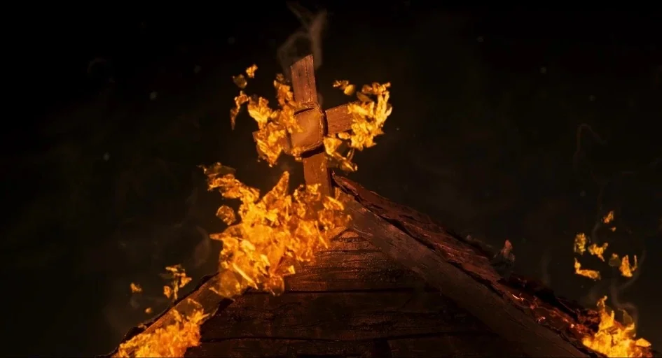 Memoir of a Snail (2024) movie still: medium — A wooden church roof with a central cross is engulfed in bright orange flames. Smoke swirls into the…