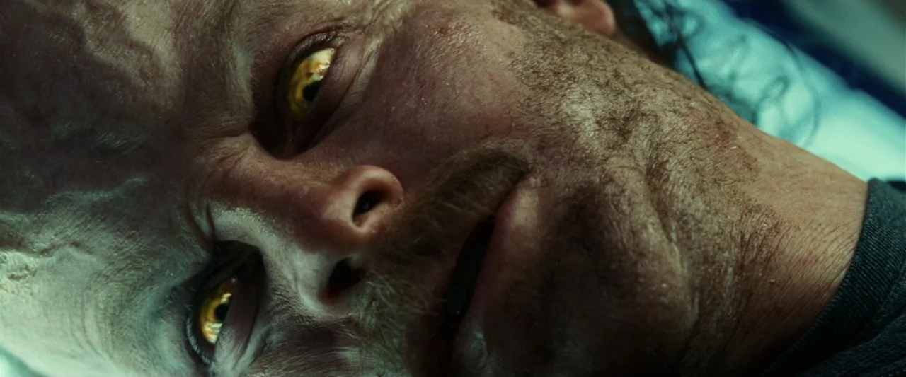 Green Lantern (2011) movie still: closeup — A close view of a man's face with textured skin and yellow irises. The subject lies supine while staring…