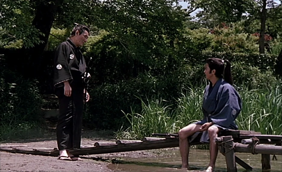 Gohatto (1999) movie still: wide — A narrow wooden footbridge crosses a small stream surrounded by dense lush green foliage. A standing older man in…