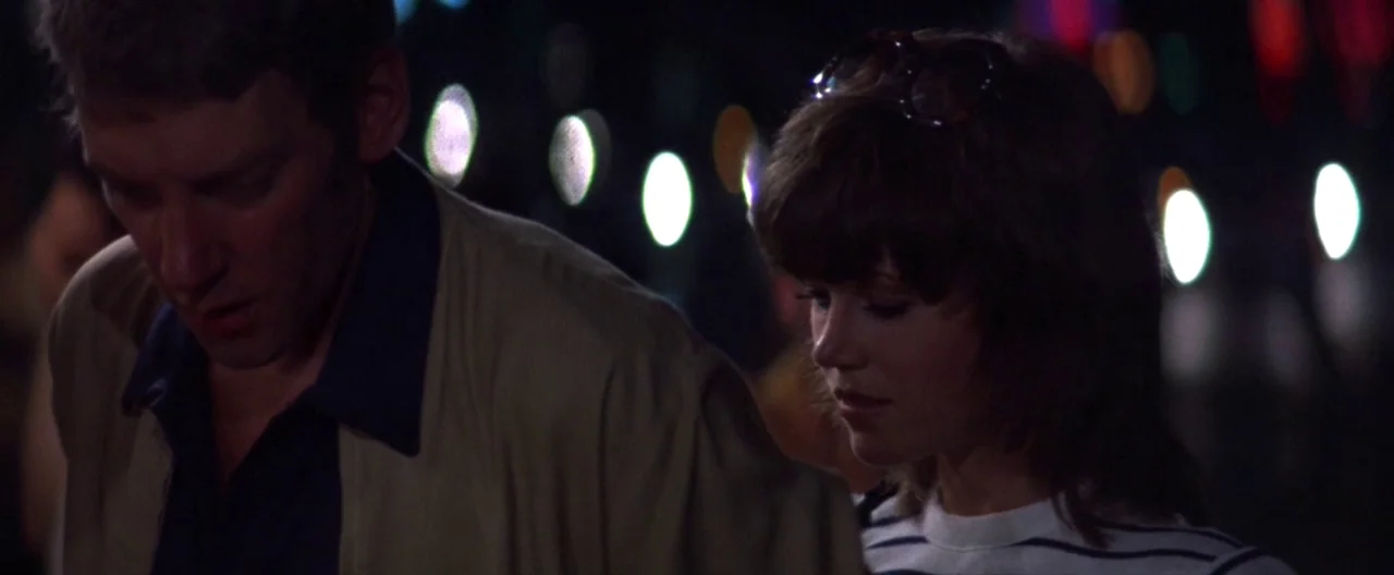 Klute (1971) movie still: medium — A dark urban environment at night with blurred city lights in the background. A man and a woman stand together…