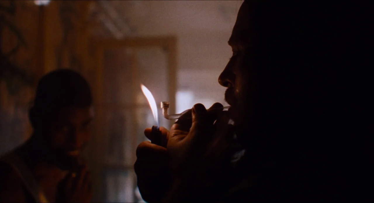 Deep Cover (1992) movie still: medium — A dark indoor space contains two men, one foregrounded and one blurred in the background. A man holds a…