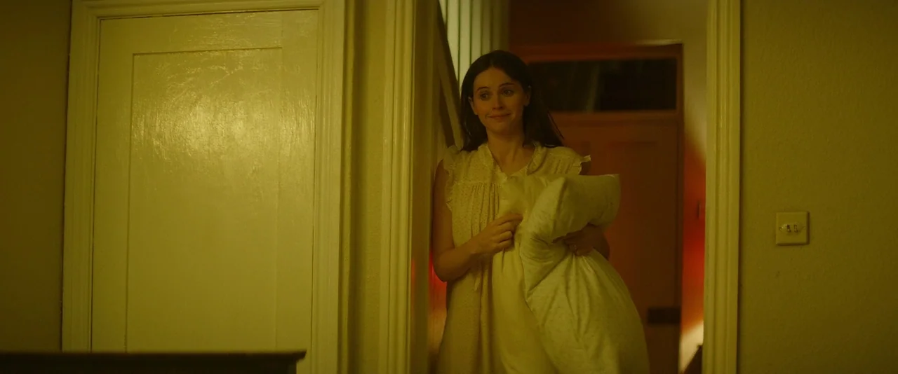 The Theory of Everything (2014) movie still: medium — A woman stands in a dimly lit hallway doorway with wooden trim. She holds a white pillow…