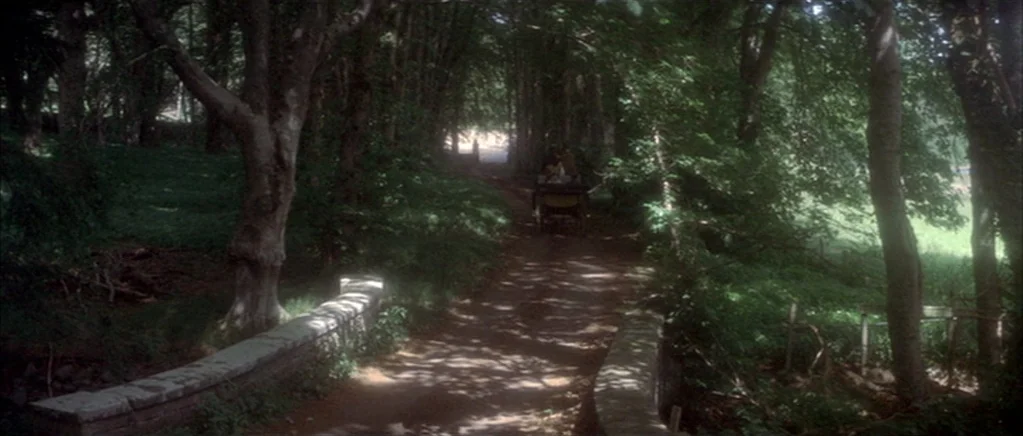 The Private Life of Sherlock Holmes movie still: wide — A stone bridge spans a small stream on a tree-lined dirt carriage path. A distant…