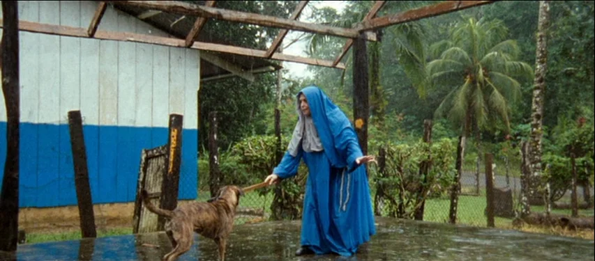 Mister Lonely (2007) movie still: fullbody — A covered concrete patio sits adjacent to a weathered building with blue painted walls. A nun in a blue…