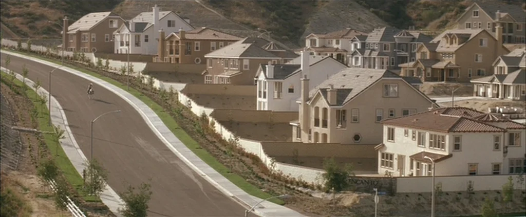 Down In The Valley (2005) movie still: establishing — A sprawling suburban housing development features rows of stucco homes with tiled roofs. A…