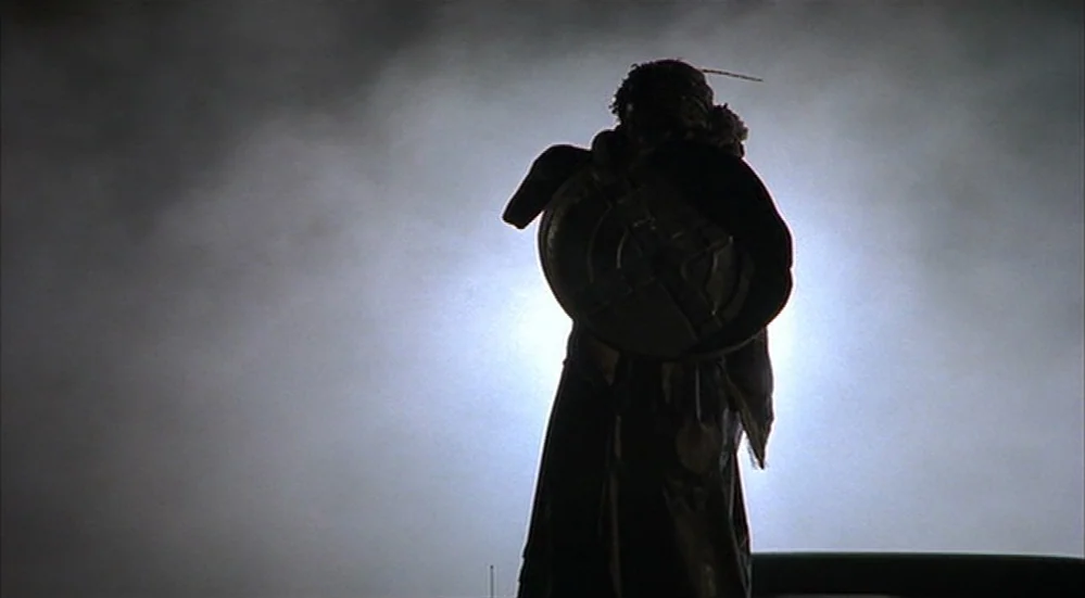 The Fisher King (1991) movie still: fullbody — A dark figure stands on a roof at night against a glowing white background. The person holds a large…