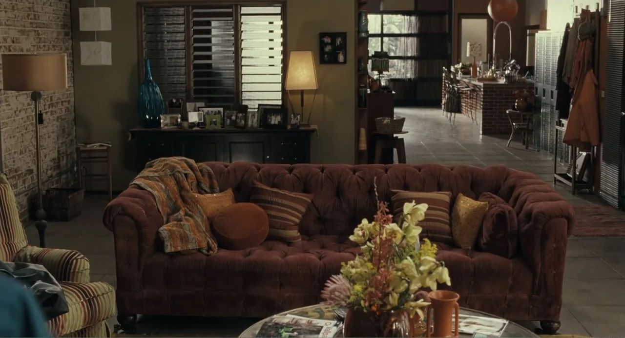 Because I Said So (2007) movie still: wide — A spacious living room features a tufted brown sofa and brick wall interior. Empty room with a coffee…