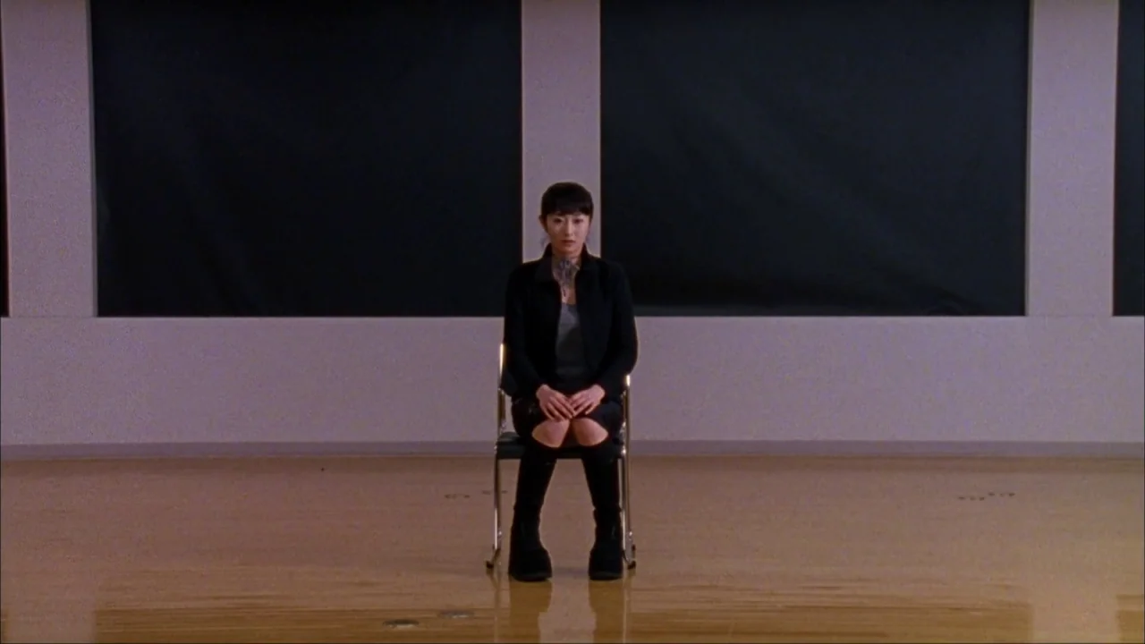 Audition (1999) movie still: medium — A minimalist studio space with polished light wood floors and large rectangular black panels. A young woman…
