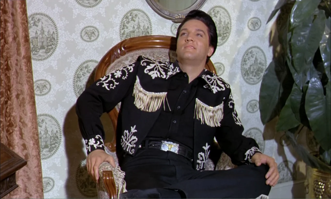 Frankie and Johnny (1966) movie still: medium — A room with patterned wallpaper and a large indoor plant sits behind an armchair. A man in a black…