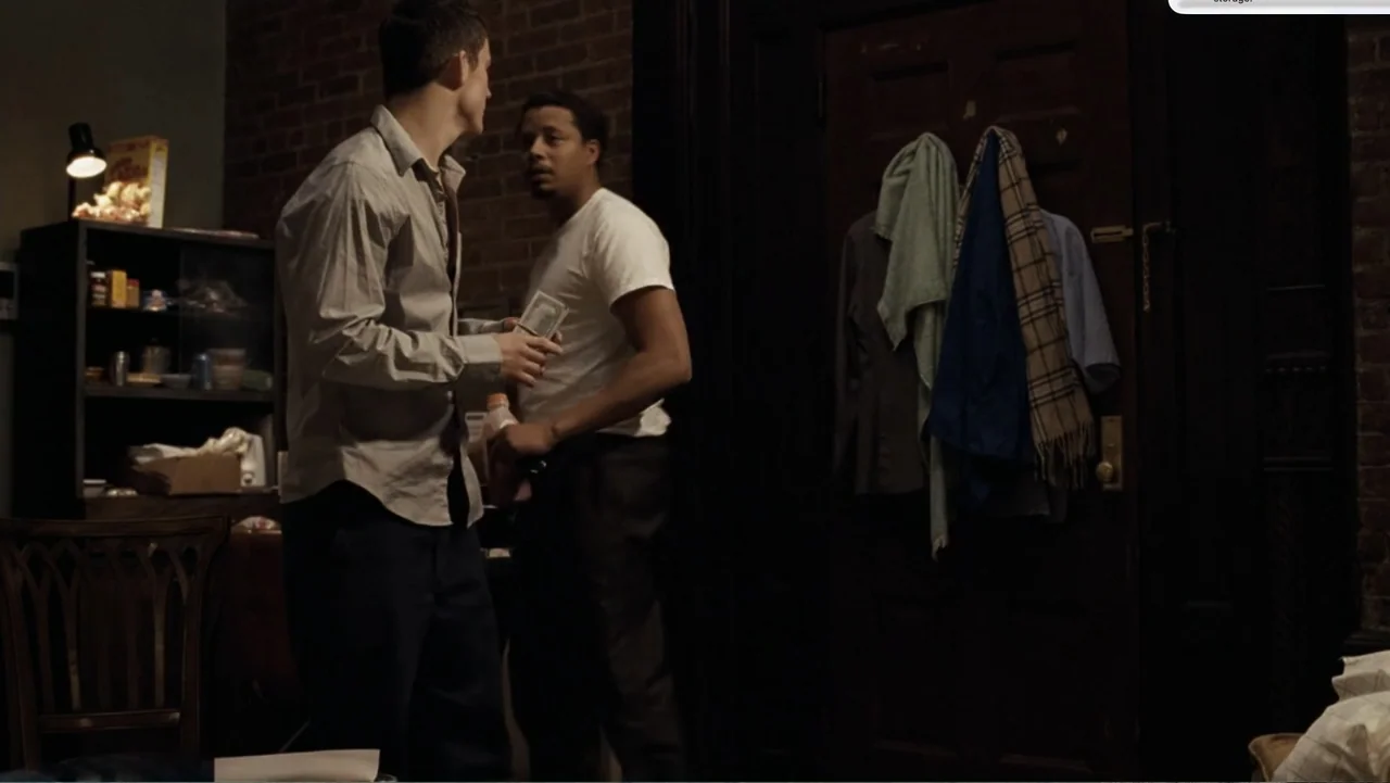Fighting (2009) movie still: medium — An interior space with a brick wall and a wooden door with hanging clothes. Two men exchange a stack of…
