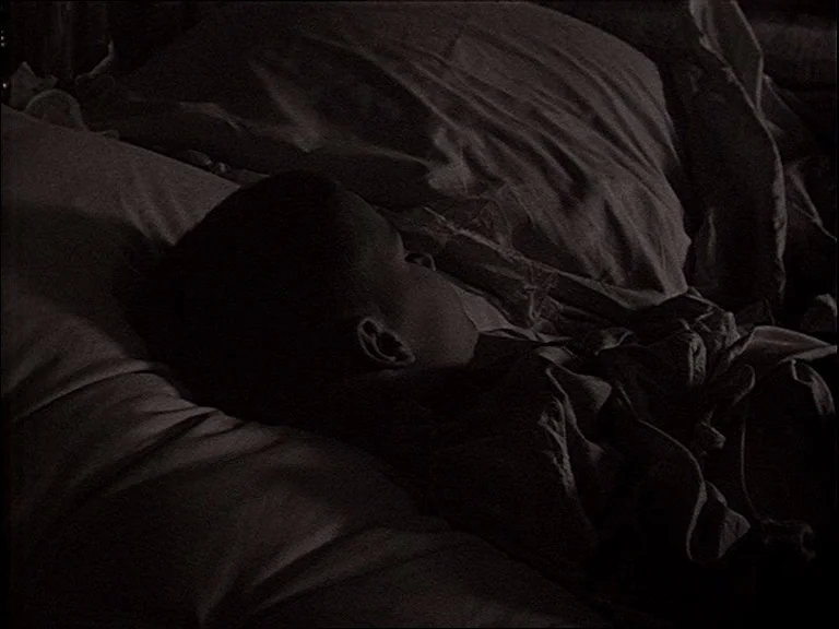 Mirror (Зеркало, Zerkalo) (1975) movie still: closeup — A dark bedroom with soft fabric bedding textures visible in low light. A child rests their…