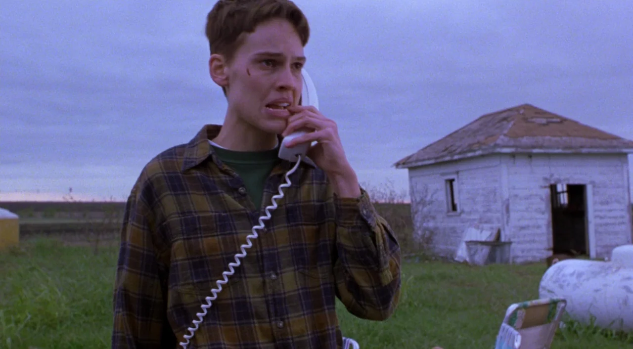 Boys Don’t Cry (1999) movie still: medium — A desolate rural landscape at dusk features a small, weathered white shed. A young woman stands in the…