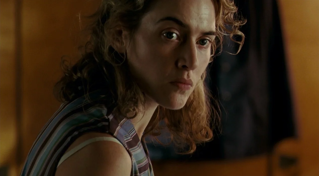 The Reader (2008) movie still: closeup — A woman stands in a room with warm-toned vertical wood paneled walls. She turns her head to look directly…
