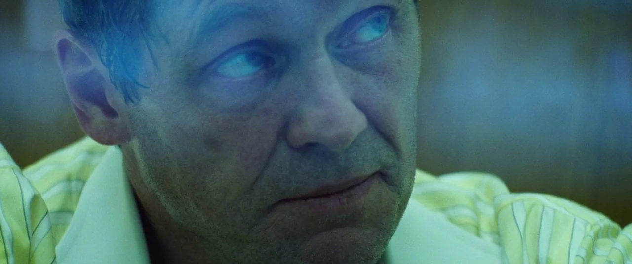 Uncut Gems (2019) movie still: closeup — A man looks at a screen in a dark, interior setting. Blue light reflects across his eyes and skin from an…