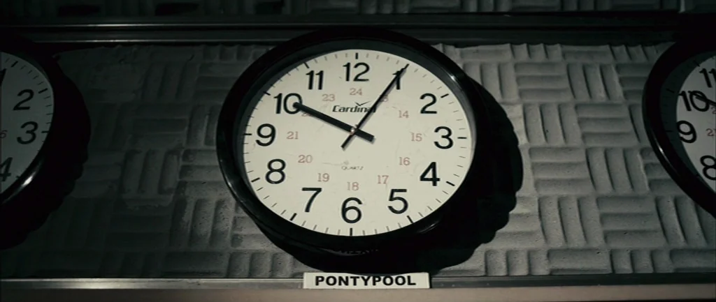 Pontypool (2008) movie still: closeup — Three analog wall clocks are mounted on a grey, textured sound-dampening acoustic wall panel. Each clock…