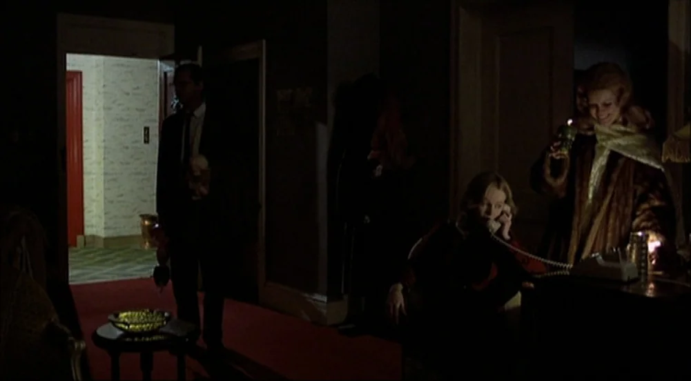 The King Of Marvin Gardens movie still: medium — A dimly lit room with dark walls and a bright hallway visible through the doorway. Three people…