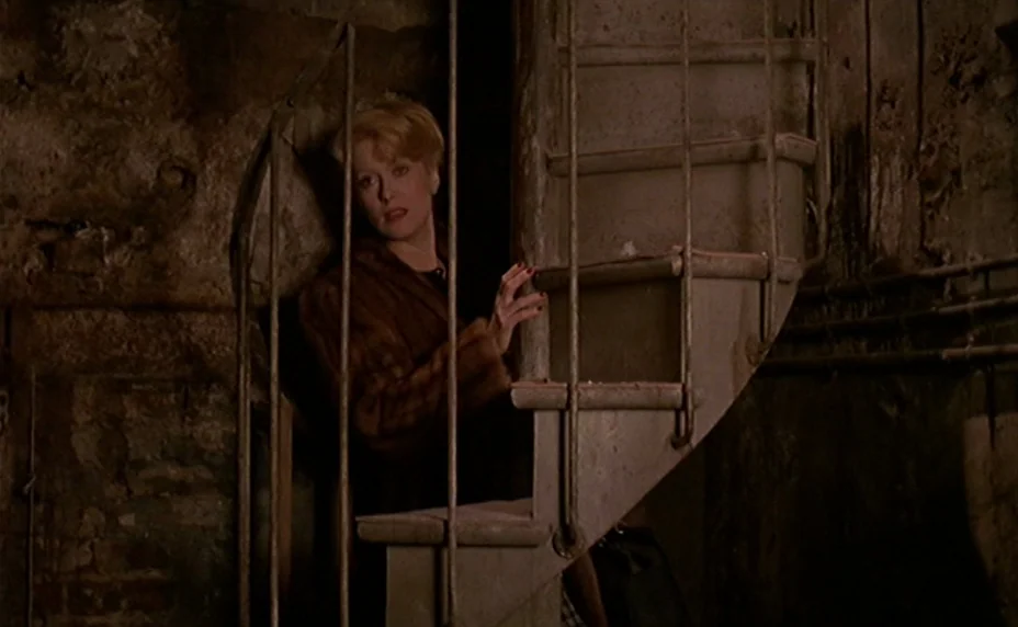 The Last Metro (1980) movie still: medium — A dark, unfinished basement features rough textured stone walls and a circular metal staircase. A woman…