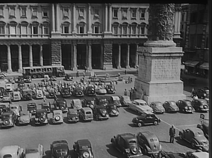 Variety Lights (1950) movie still: establishing — A crowded public square in Rome features a large classical column on a pedestal. Many vintage…